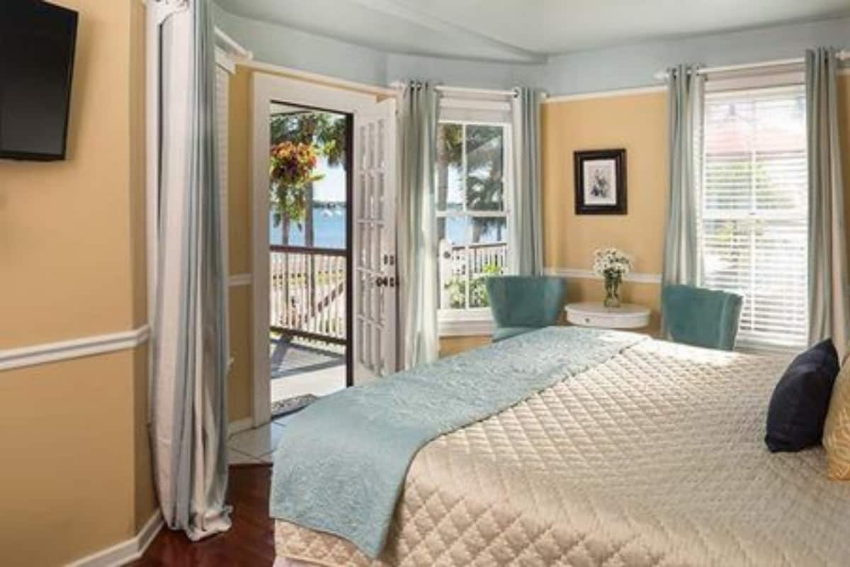 A bedroom with a bed, a chair, a small table, and a window with curtains.