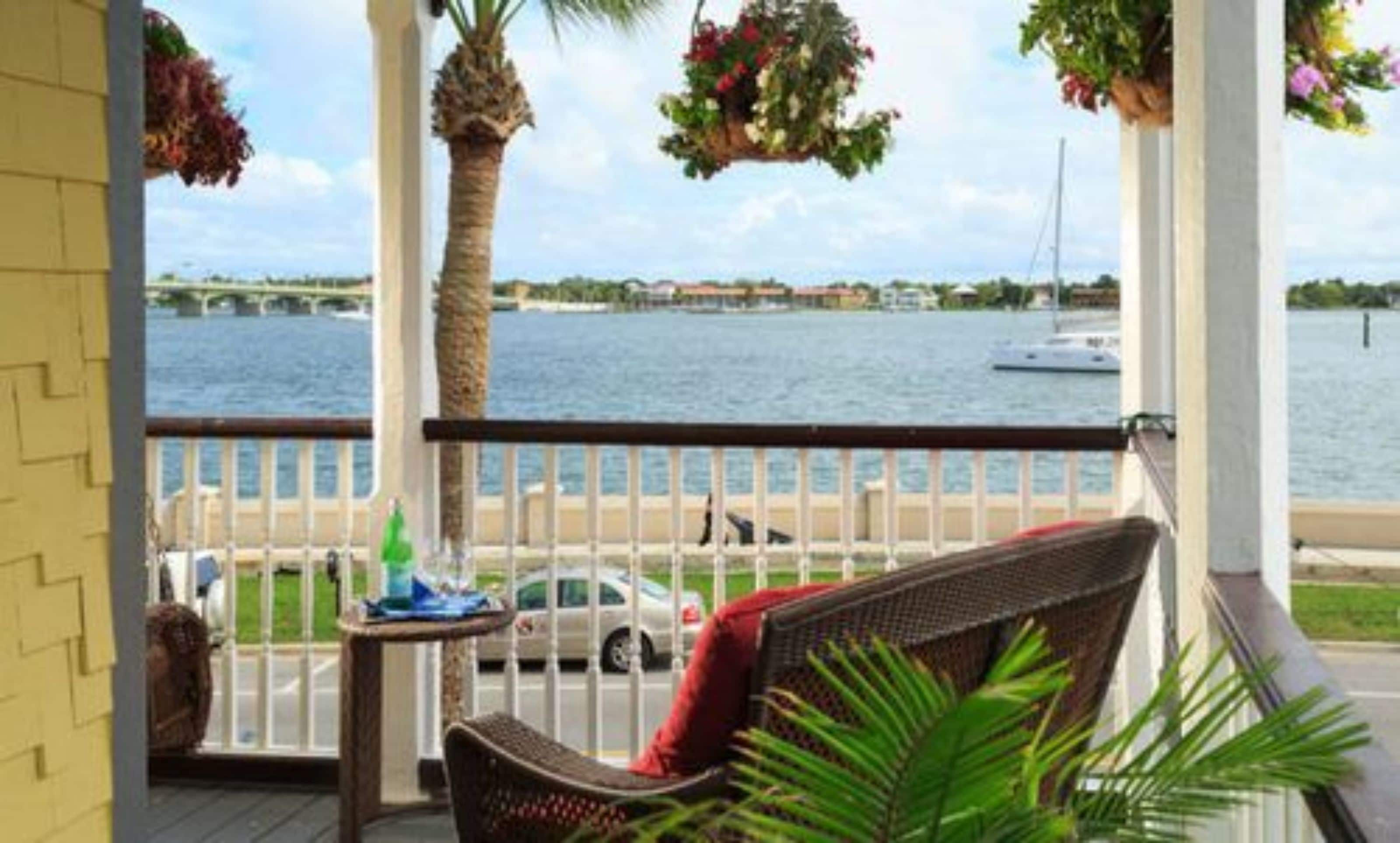 A balcony with wicker furniture, a view of the water, and hanging flower baskets.