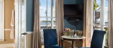 A room with two blue chairs, a small round table with a vase of flowers, and a television mounted on the wall.