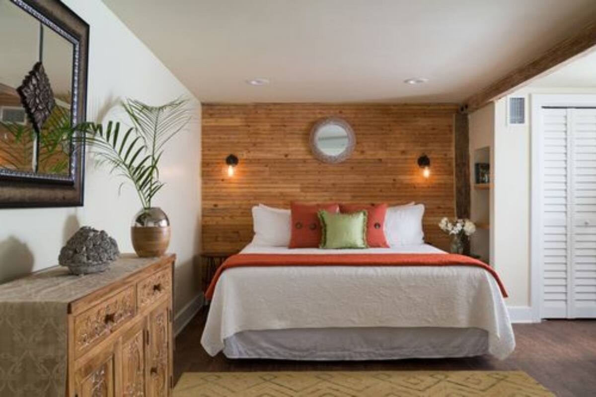 A bedroom with a wooden headboard, a large bed with white bedding, a mirror, and a potted plant.