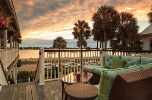 A wooden deck with a wicker sofa and a glass table, overlooking a road with parked cars and palm trees. - Bayfront Marin House (St. Augustine)