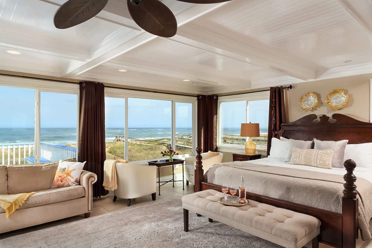 A spacious bedroom with a large bed, a seating area with a view of the ocean, and a balcony with a table and chairs.