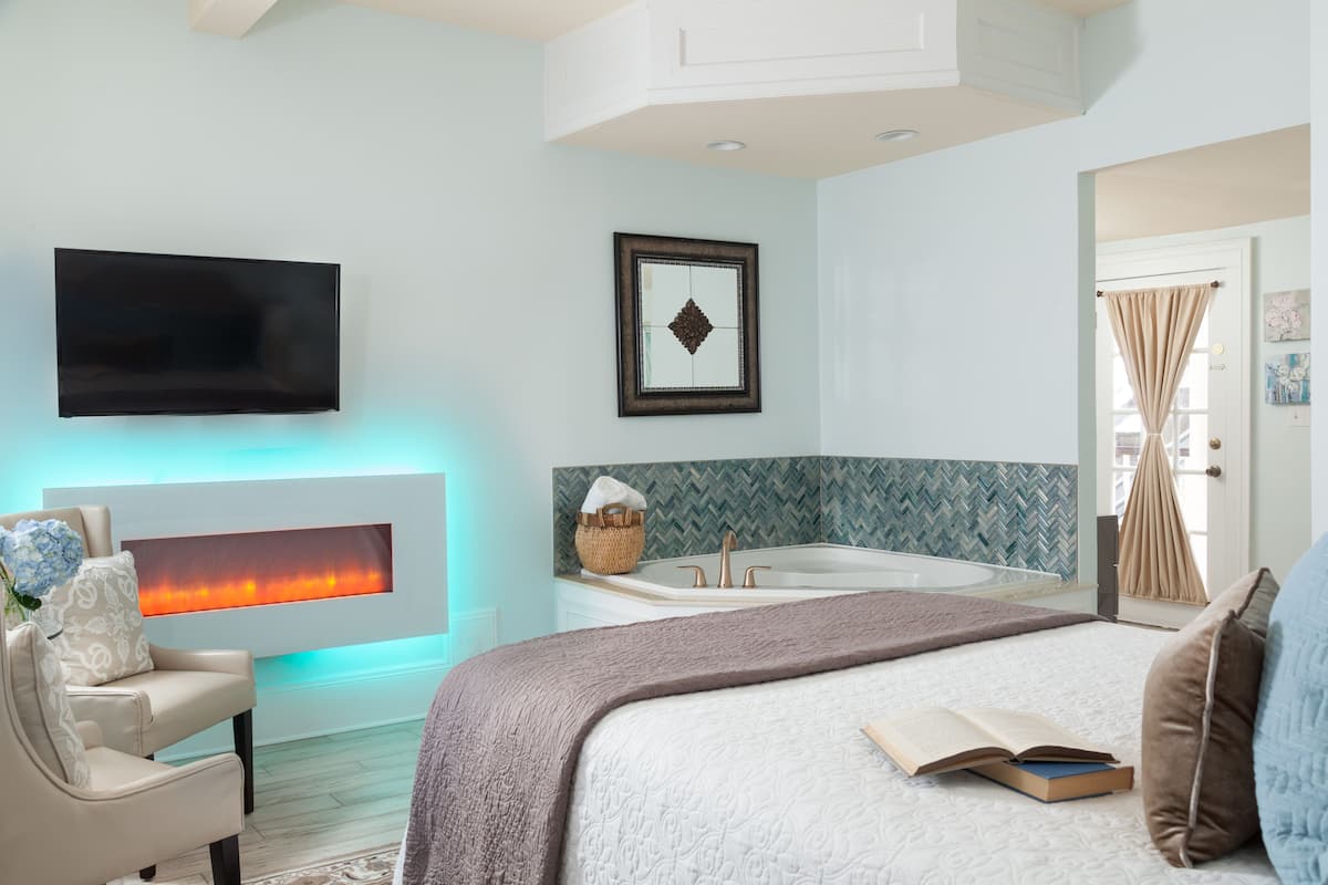 A bedroom with a bed, a TV, a fireplace, a bathtub, and a window with curtains.