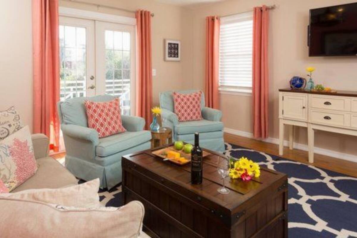 A living room with two light blue sofas, a wooden coffee table with a bottle and fruit, a white cabinet, and a TV mounted on the wall.
