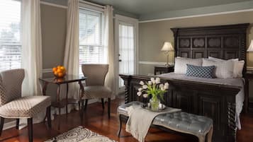 Un dormitorio con una cama grande, dos sillas, una mesita con fruta, un banco y una ventana con cortinas.