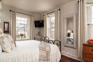 A bedroom with a bed, a television, a mirror, and a dresser with a fruit basket. - Bayfront Marin House (St. Augustine)