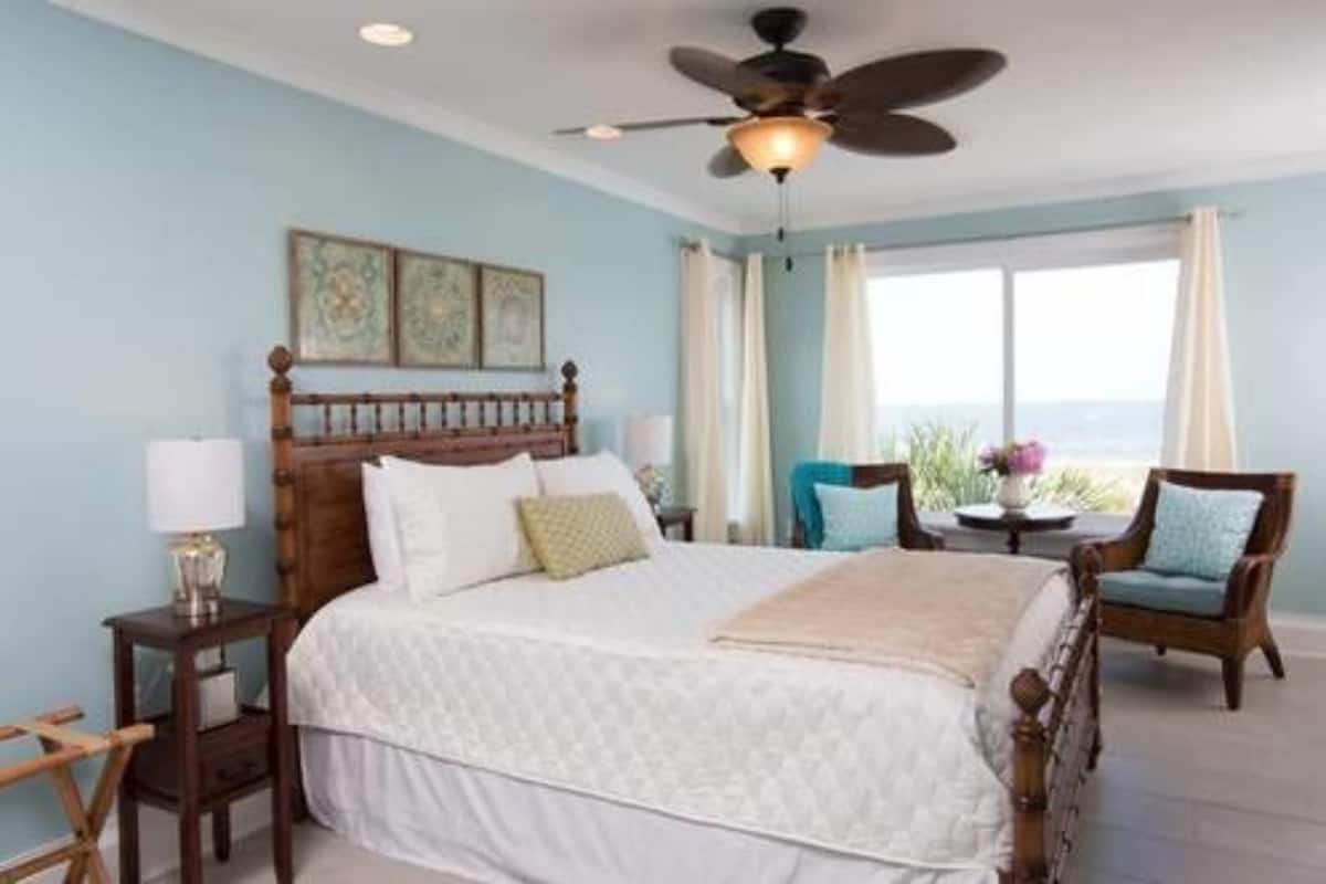 A bedroom with a bed, a ceiling fan, a nightstand, a chair, and a window with curtains.