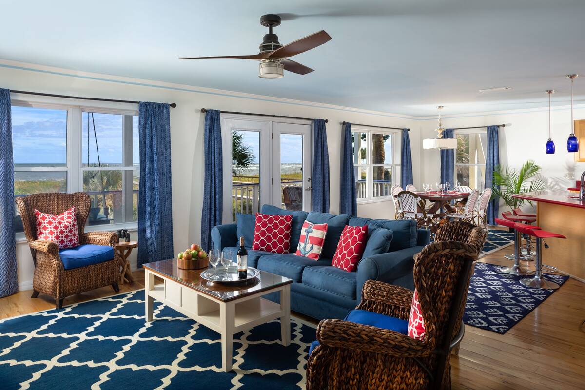 A living room with a blue sofa, wicker chairs, a coffee table, and a view of the ocean.