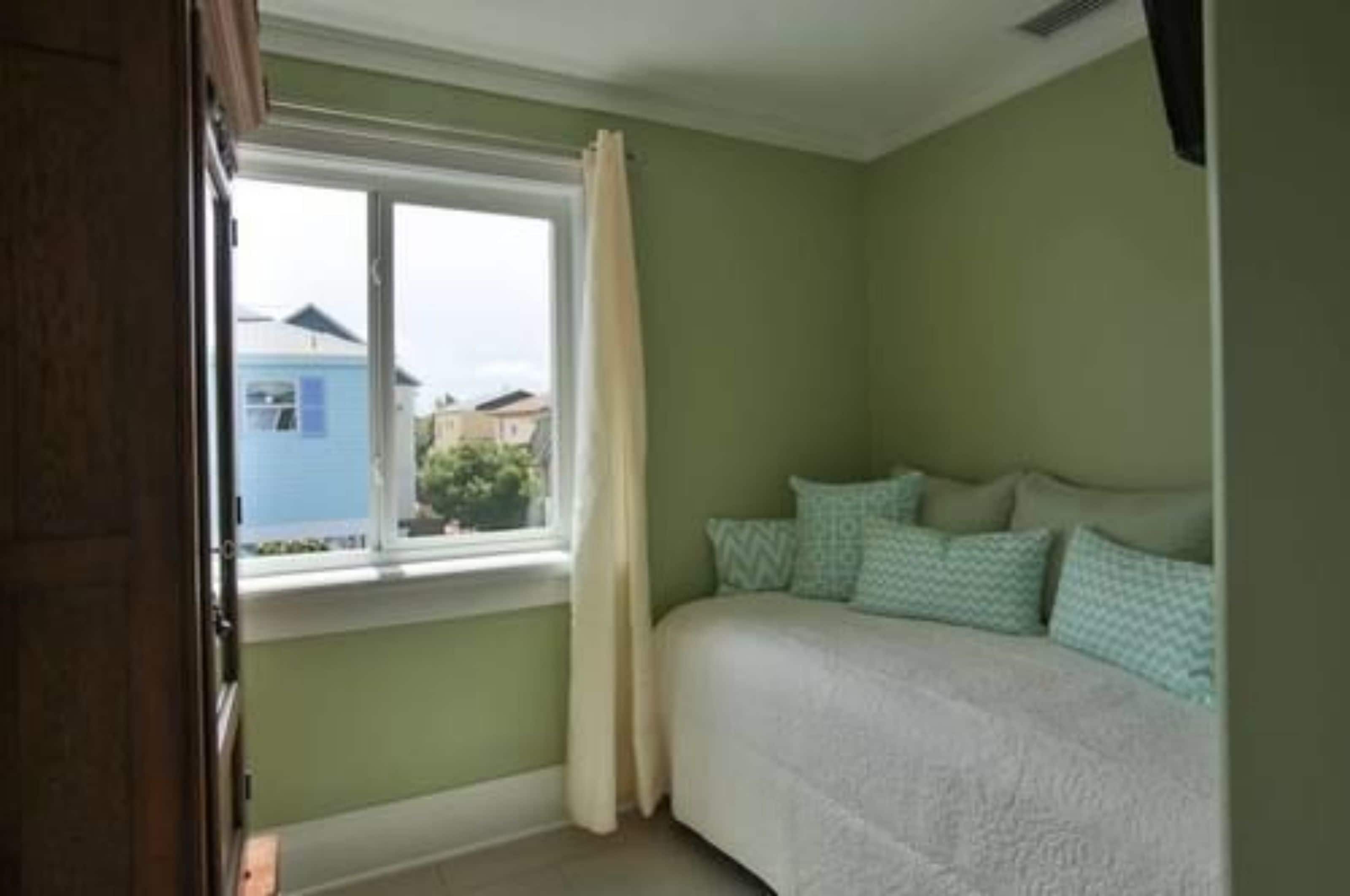 Ein Schlafzimmer mit Bett, einem Fenster mit Vorhängen und Blick auf Häuser.