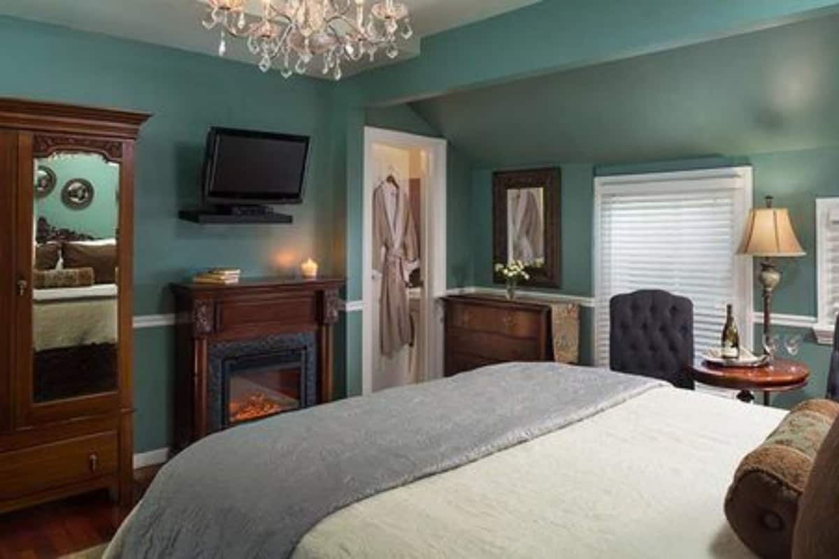 A bedroom with a bed, a television, a fireplace, and a chandelier.