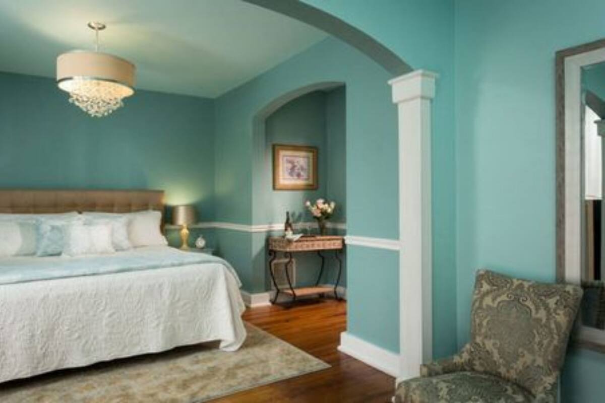 A bedroom with a bed, a nightstand, a chair, and a picture frame on the wall.