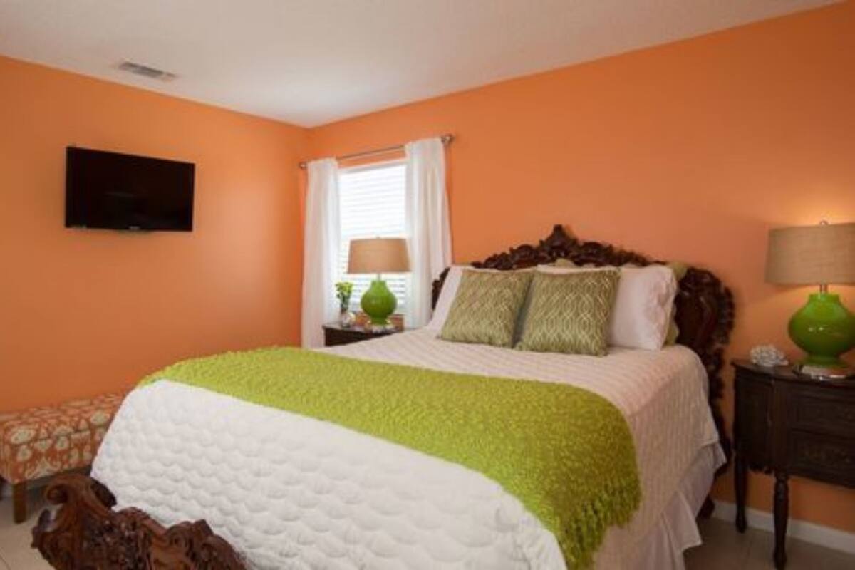 A bedroom with a bed, a television on the wall, and a window with curtains.