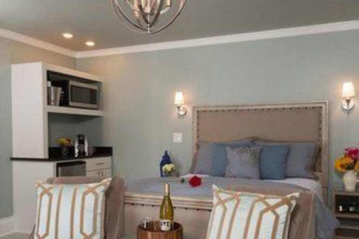 A bedroom with a bed, two armchairs, a small table, and a chandelier.