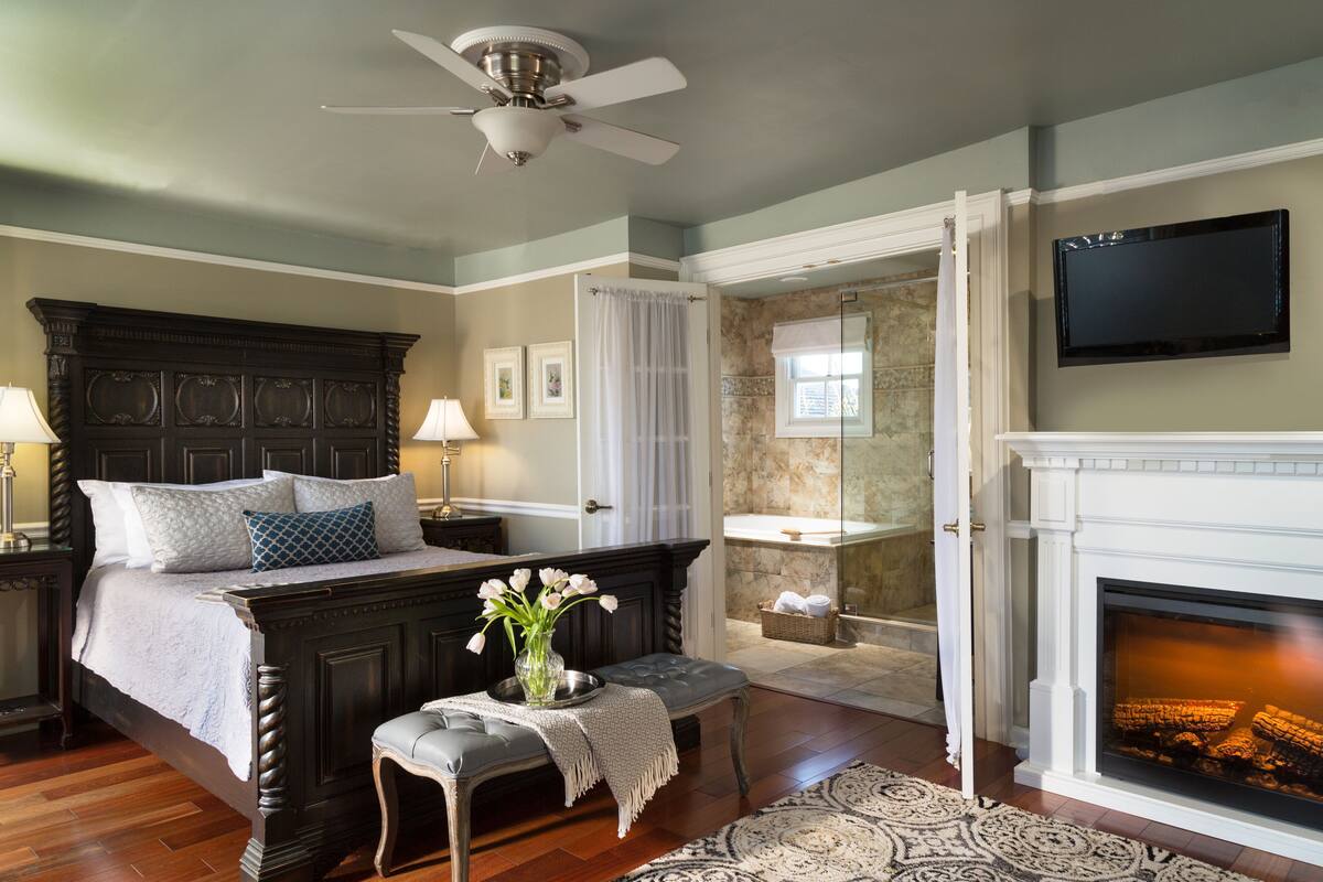 A bedroom with a large bed, a bench, a fireplace, and a television.