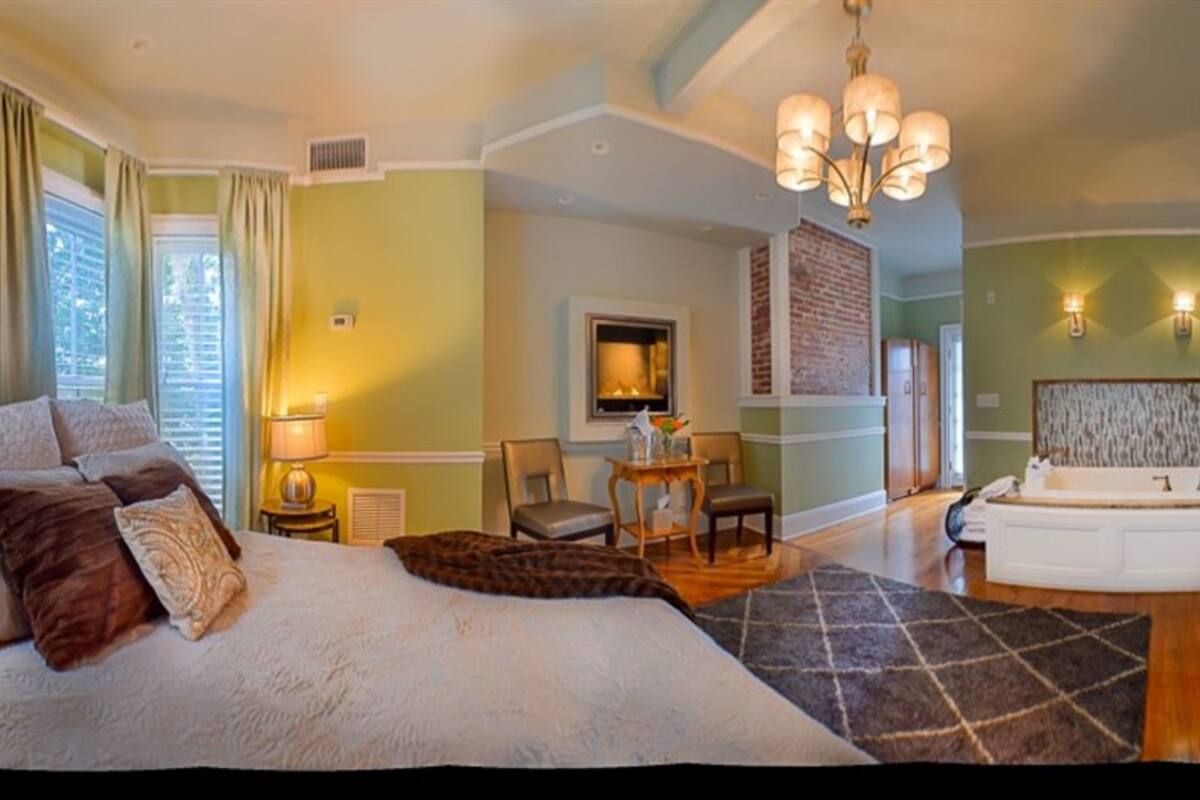 A spacious bedroom with a large bed, a sitting area with a table and chairs, a fireplace, and a separate bathroom with a bathtub.