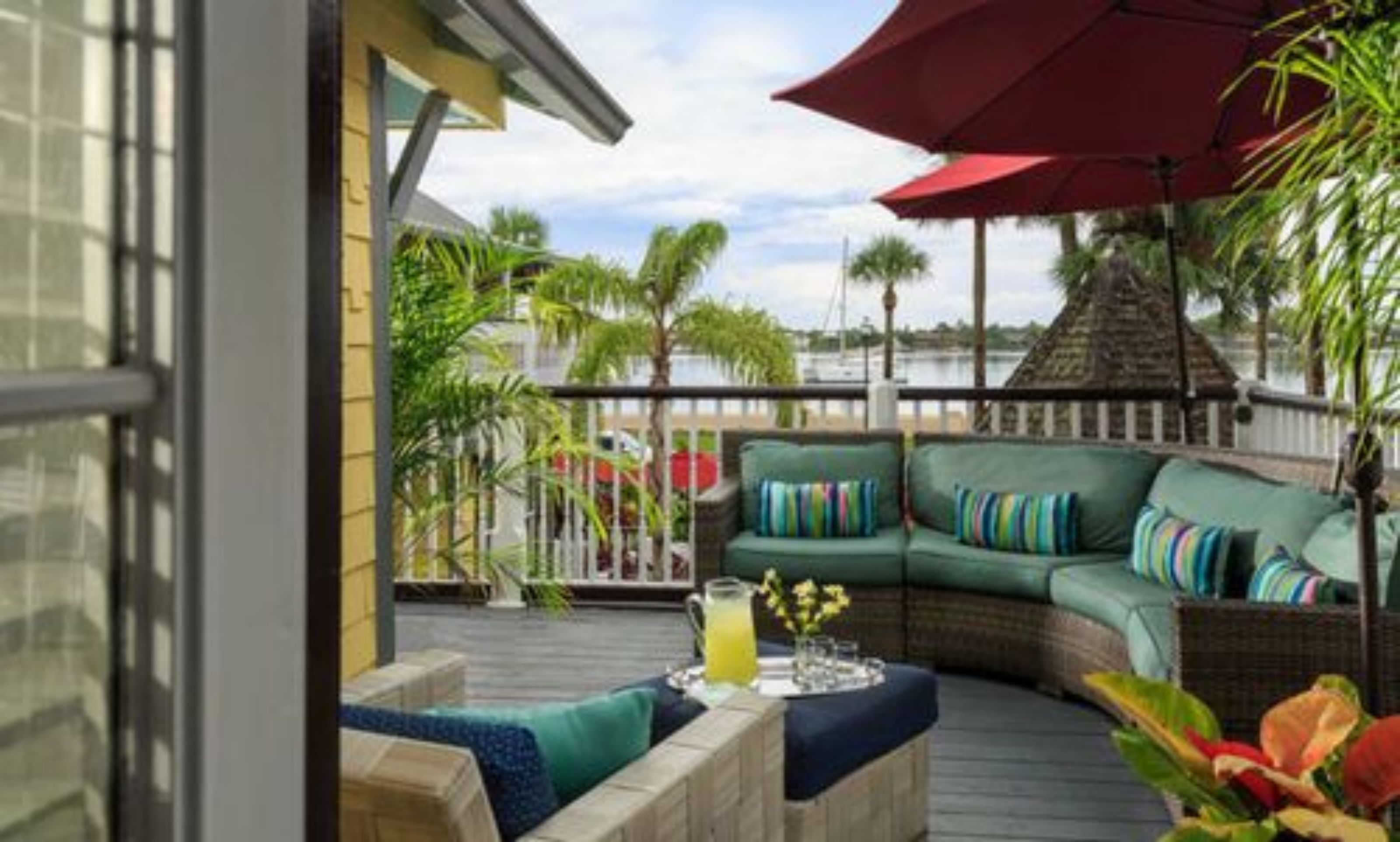 Eine Terrasse mit einer grünen Couch, einem roten Sonnenschirm und einem Holztisch mit einem Getränk.