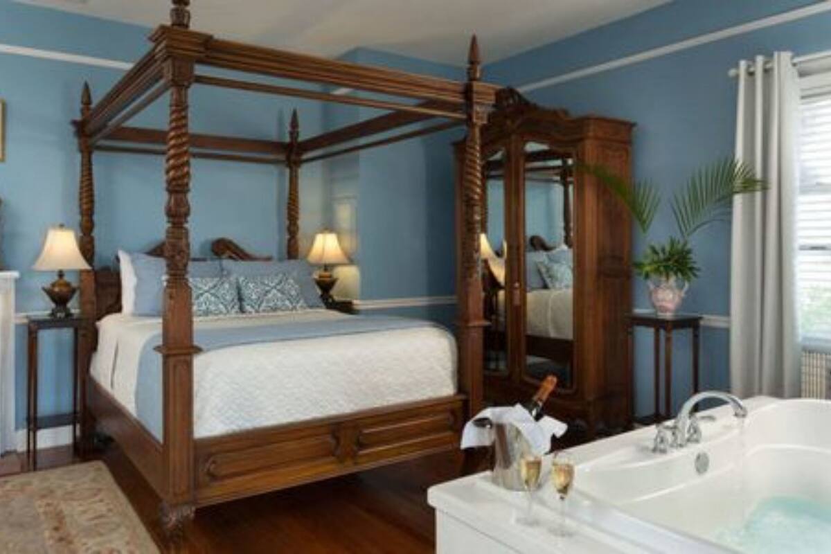 A four-poster bed with a wooden canopy, a white bathtub with a champagne bottle and glasses, and a mirror on the wall.