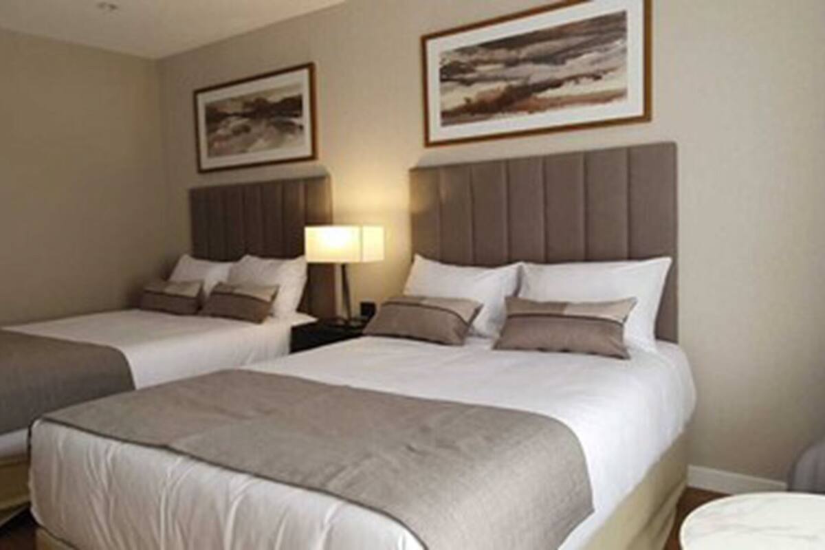 A hotel room with two beds, a nightstand with a lamp, and two framed pictures on the wall.