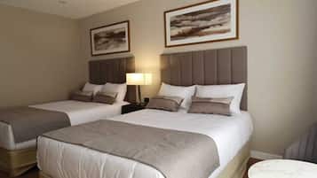 A hotel room with two beds, a nightstand with a lamp, and two framed pictures on the wall.