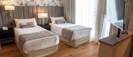 Quarto de hotel com duas camas, televisão, escrivaninha e mesa de cabeceira.