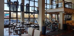 A spacious indoor area with multiple tables and chairs, large windows, and a staircase leading to an upper level. - Albatros Hotel (Ushuaia)