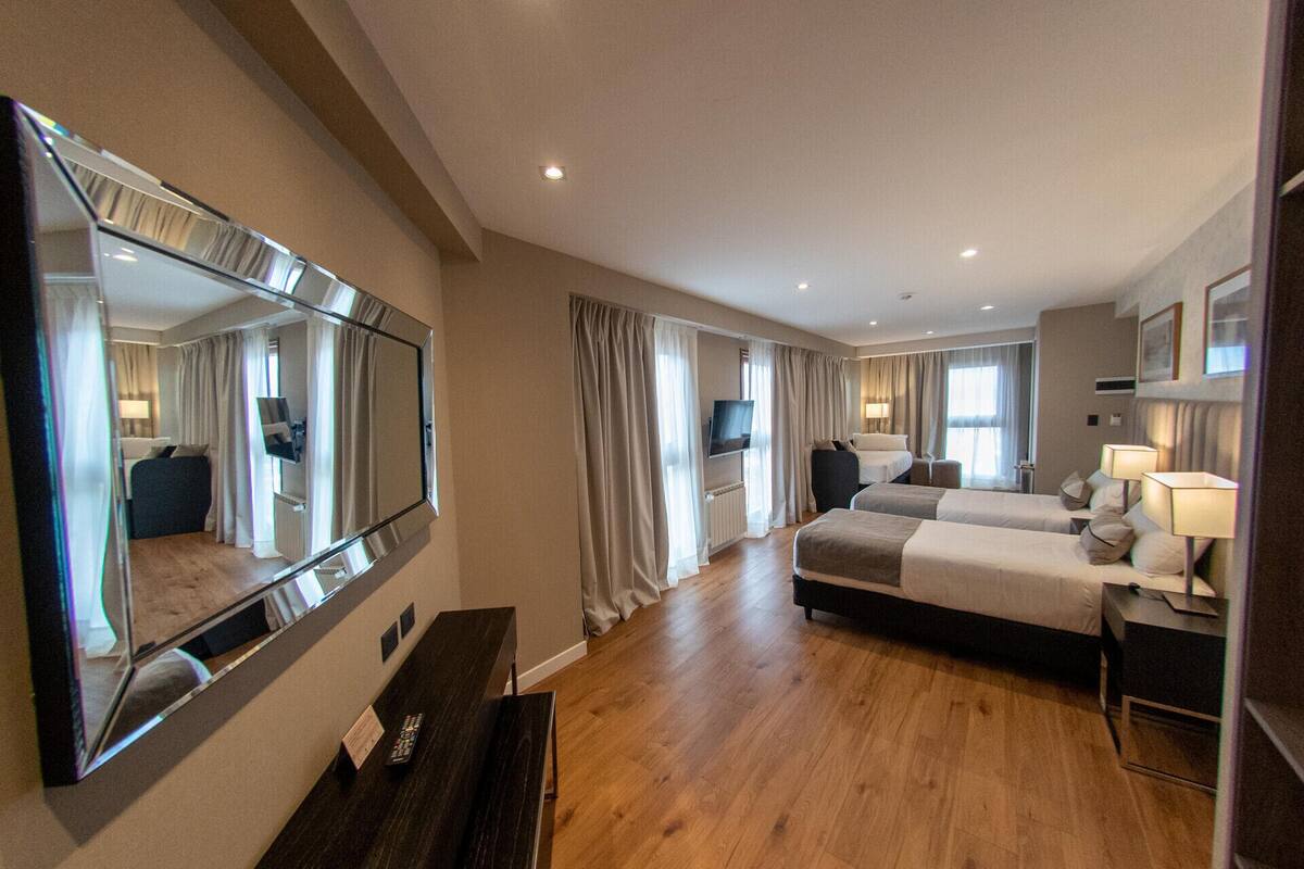 A hotel room with a large mirror, two beds, a TV, and a desk with a remote control.