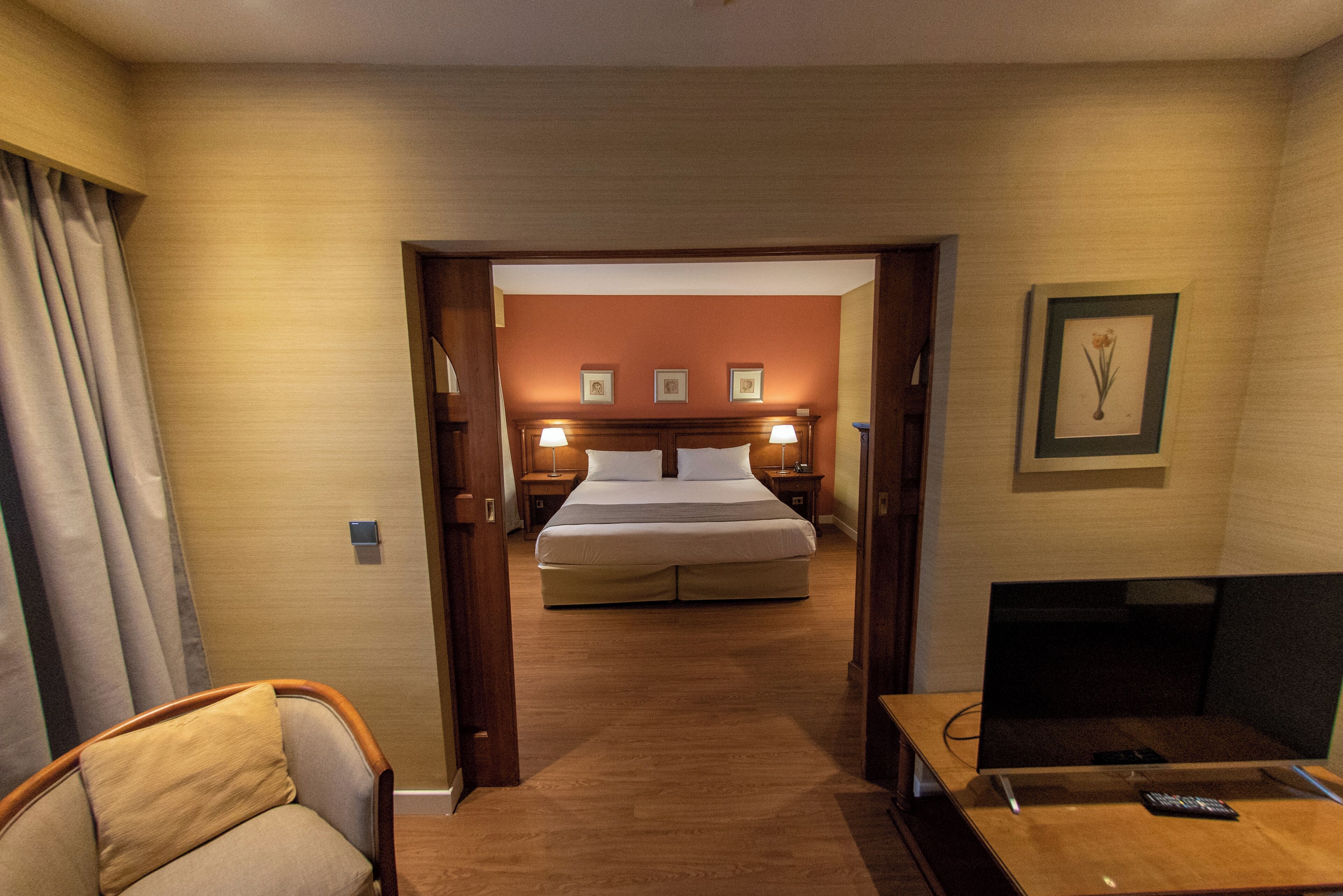 A hotel room with a bed, bedside tables, a desk with a chair, and a television.