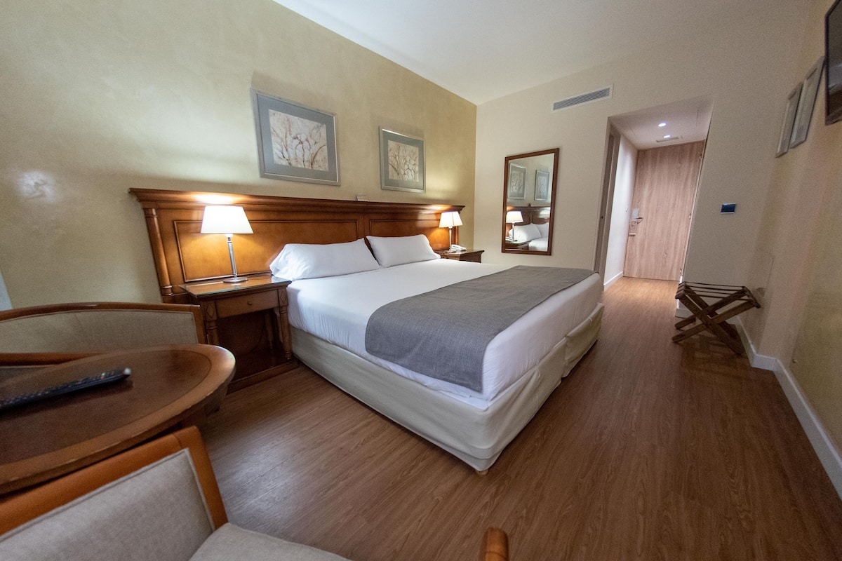 A hotel room with a bed, bedside tables, a chair, and a wooden floor.