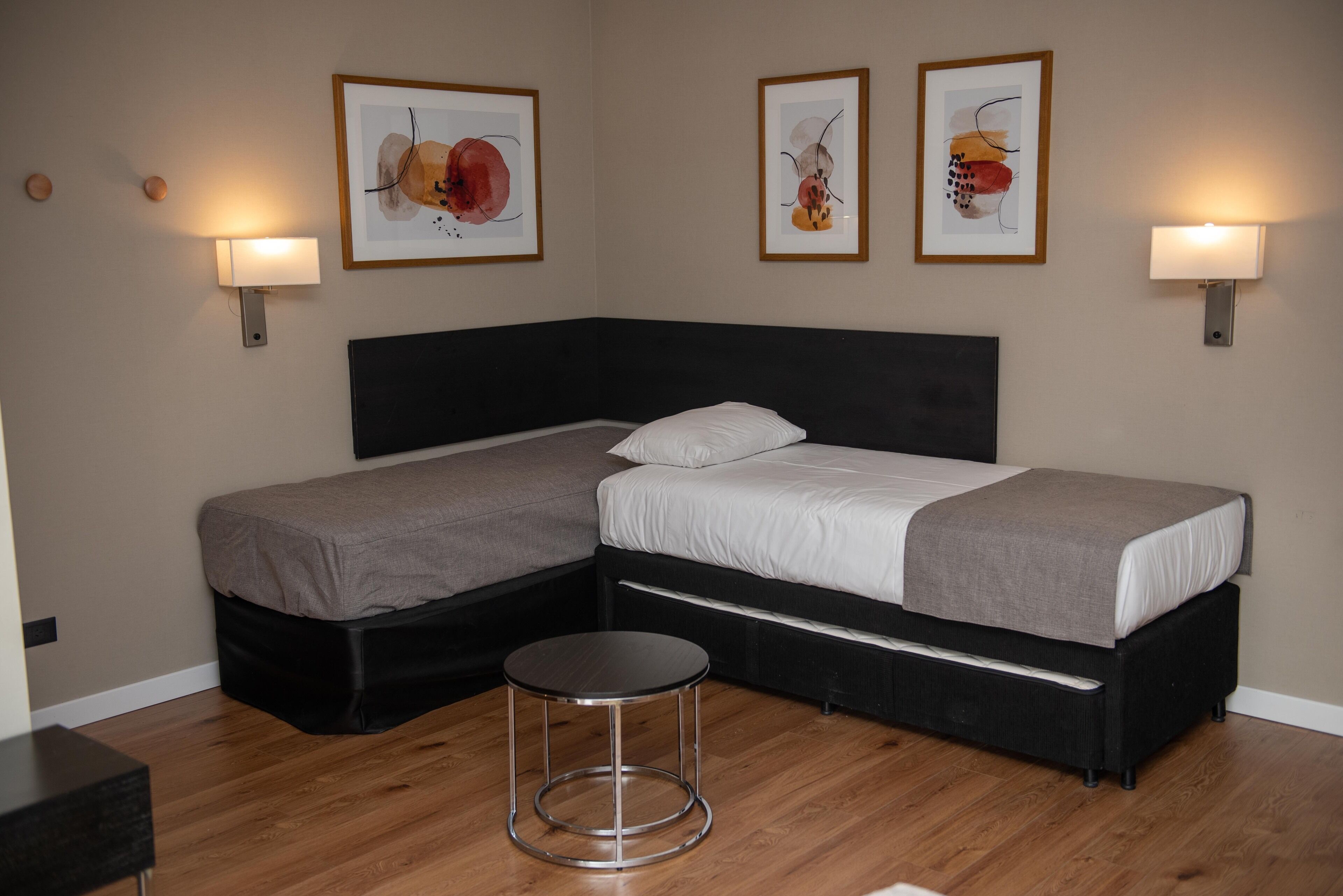 A double bed with a black headboard, a round stool, and two framed artworks on the wall.