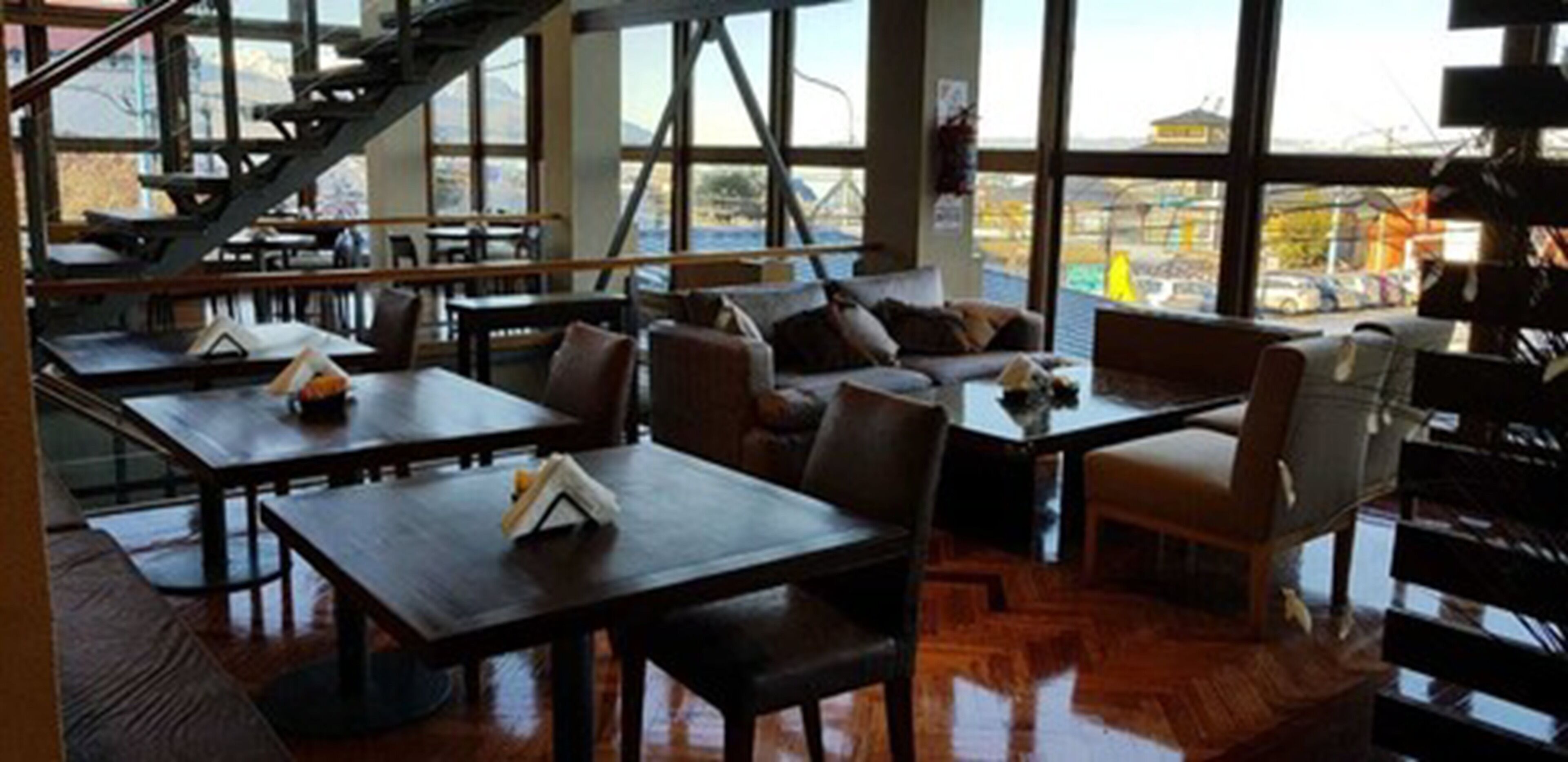 Un restaurante con mesas y sillas de madera, con grandes ventanales que ofrecen vistas al exterior.