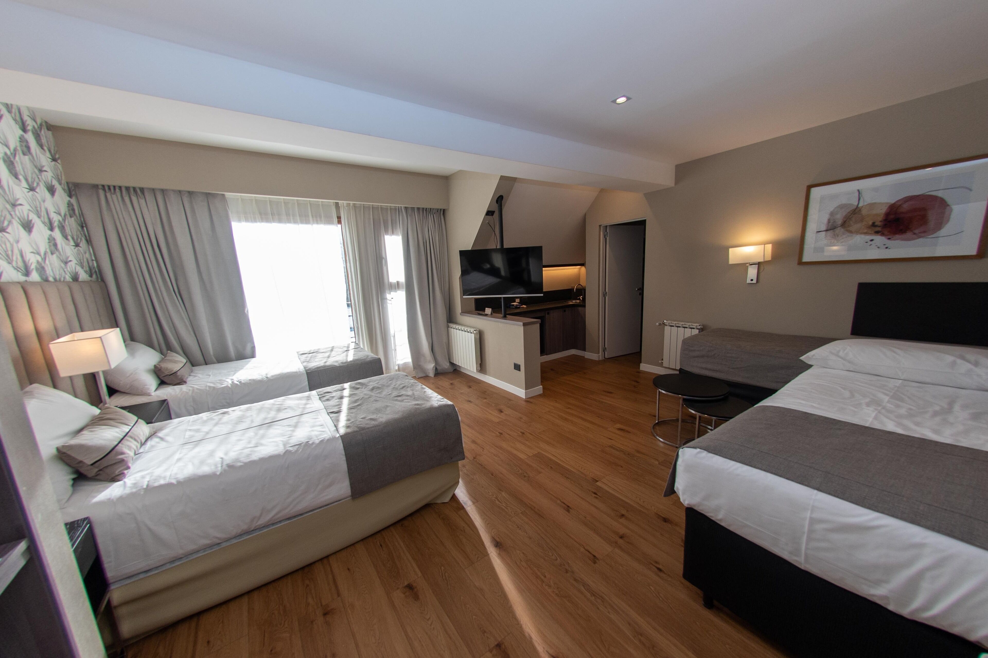 A hotel room with two beds, a desk, a TV, and a dining area.