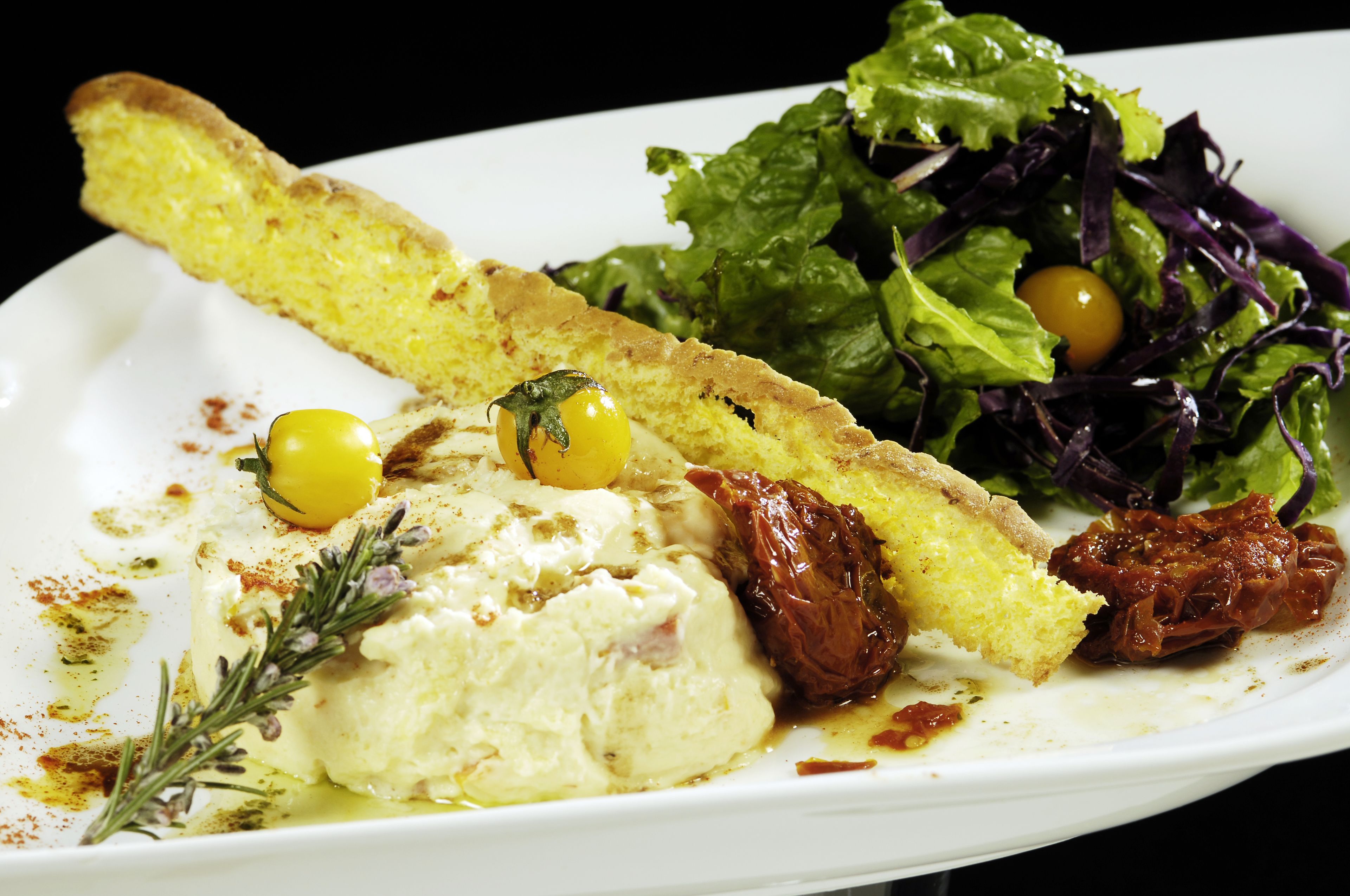 A plate with a slice of bread, a dollop of cream, a cherry tomato, and a salad.