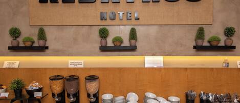 Zona de recepción de un hotel con un cartel que dice "ALBATROS HOTEL" y una mesa de buffet con diversos platos y utensilios.