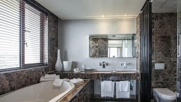 A modern bathroom with a marble countertop, a large bathtub, a glass shower enclosure, and a toilet.