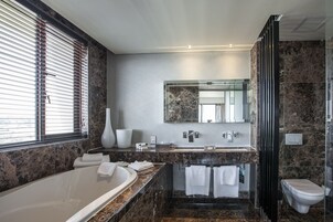 Un baño moderno con encimera de mármol, una bañera grande, una cabina de ducha de vidrio y un inodoro.