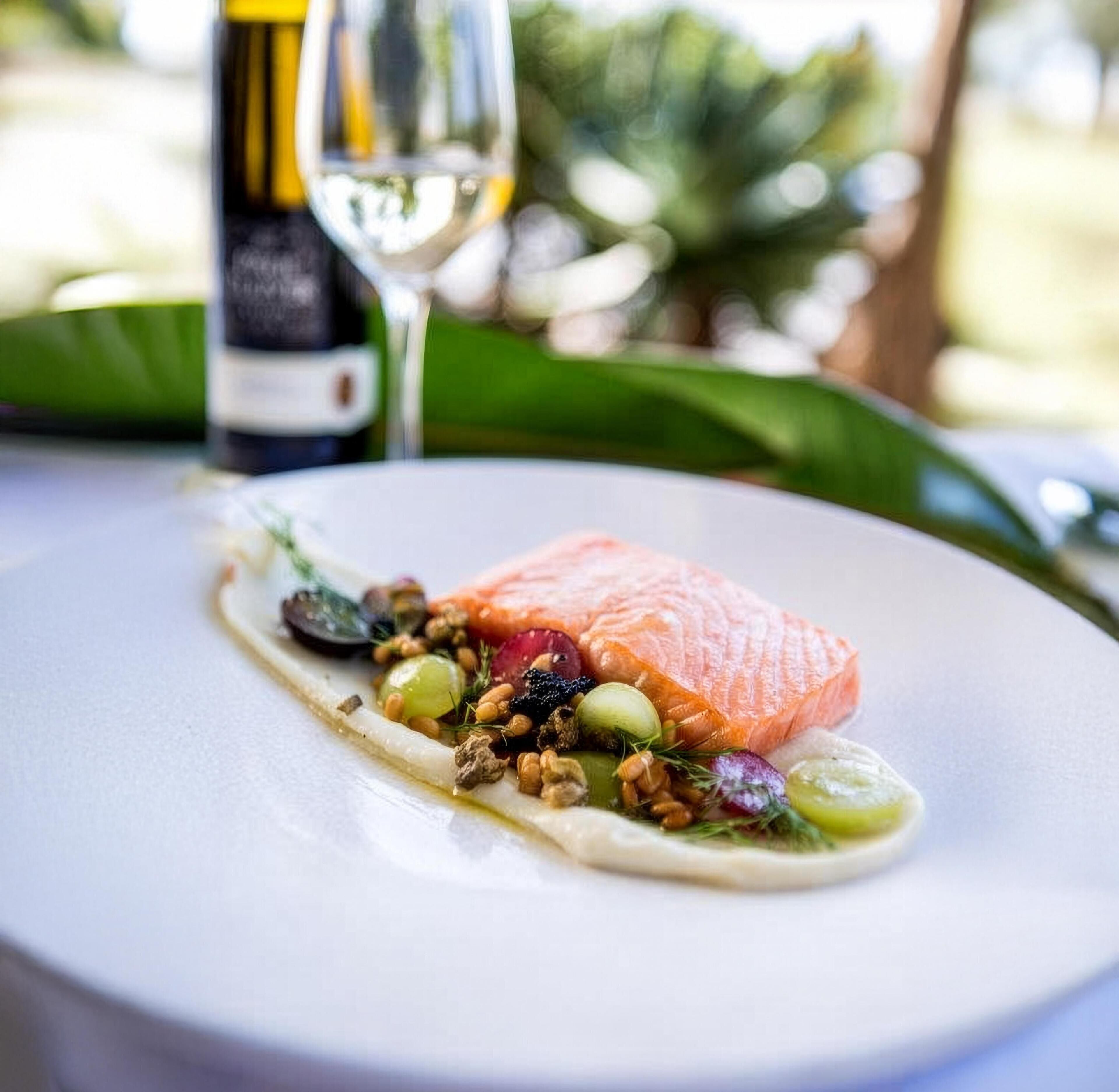A plate with a piece of salmon, nuts, and vegetables.