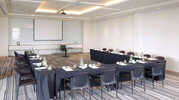 Una sala conferenze con un lungo tavolo, sedie, uno schermo per proiettore e una lavagna.