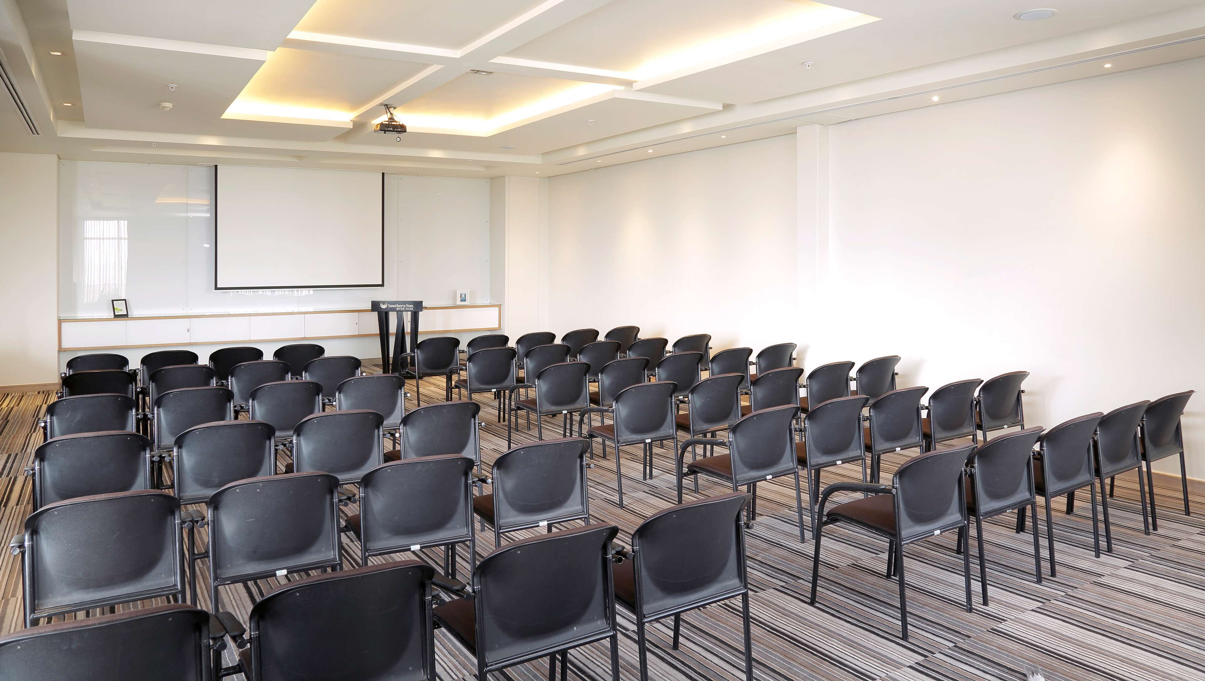 A conference room with rows of black chairs, a whiteboard, and a projector on the ceiling.
