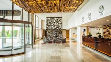 A modern lobby with a glass revolving door, a reception desk with a wooden panel design, and a geometric decorative wall.