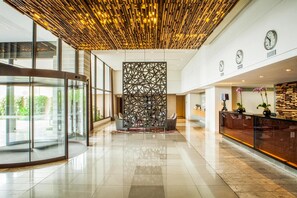 Un hall d’entrée moderne doté d’une porte tournante en verre, d’un comptoir de réception avec un décor en panneaux de bois et d’un mur décoratif aux motifs géométriques.