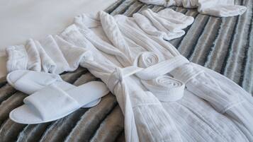A neatly arranged set of white towels and a pair of white slippers on a striped bedspread.