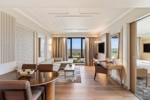 Ein Hotelzimmer mit einer Couch, einem Esstisch, einem Fernseher und Blick auf die Stadt.