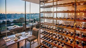 Un comedor moderno con una vinoteca llena de botellas, ventanas amplias que ofrecen vistas a la ciudad y una mesa dispuesta para comer.
