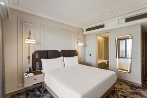Una habitación de hotel con una cama grande, mesitas de noche, un espejo y un baño visible a través de una puerta abierta.