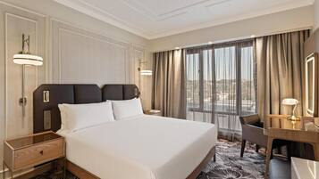Une chambre d’hôtel avec un grand lit, un bureau, une chaise, une table de chevet et une fenêtre avec des rideaux.