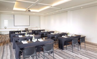 A conference room with multiple tables and chairs, equipped with nameplates, water bottles, and a projector screen.