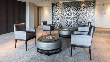 Un área de estar moderna con sillones y otomanas tapizados en gris, una pared decorativa y piso alfombrado.