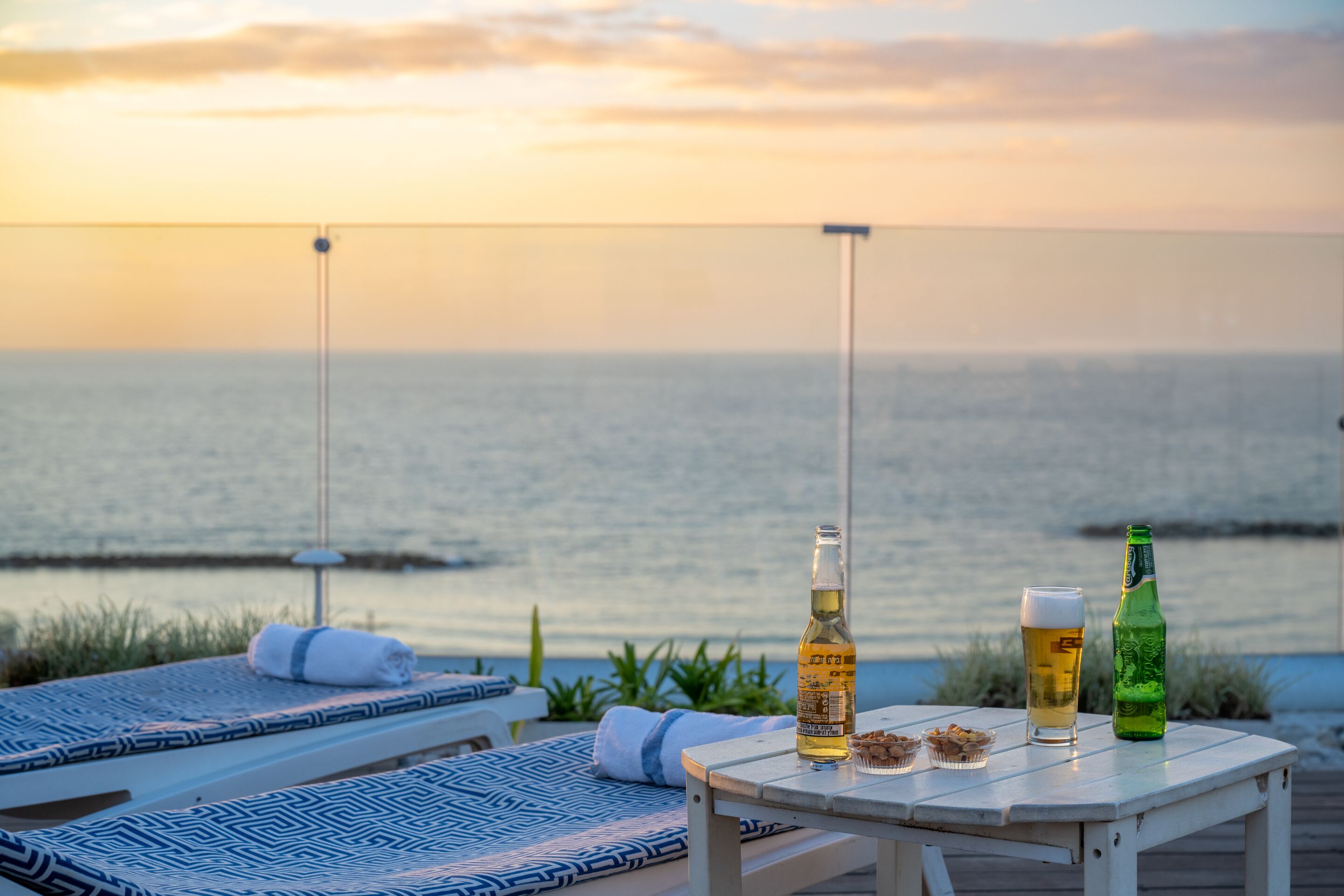 Una mesa con una botella de cerveza, un vaso de cerveza y un aperitivo con vista al mar.