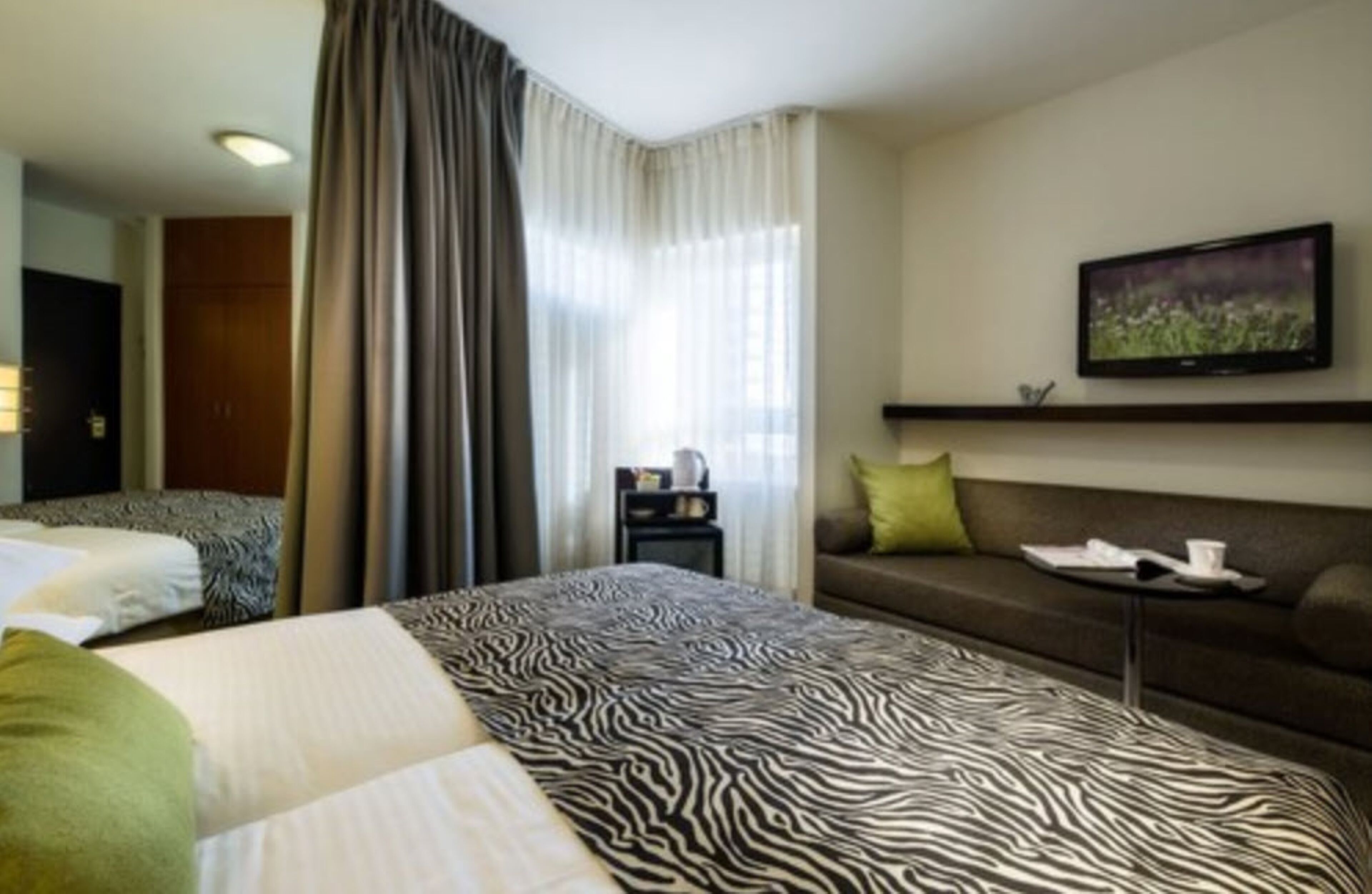 Una camera d'albergo con una coperta a motivi zebrati, un divano, una TV a schermo piatto e un piccolo tavolino con vassoio.