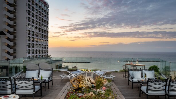 A rooftop terrace with outdoor seating, a small rock garden, and a view of the ocean at sunset. - Maxim Hotel Tel Aviv (Tel Aviv)